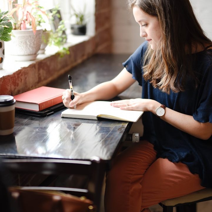 ADHD, Autism, Dyslexia Screening Woman writing in a notebook at a table with a coffee cup and books nearby.