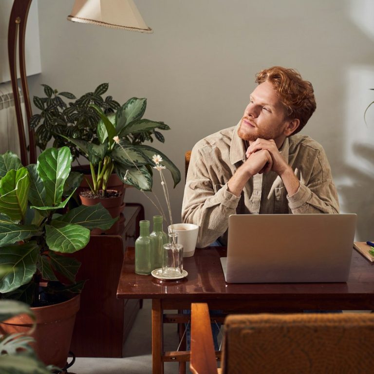 ADHD, Autism, Dyslexia Screening Person with red hair sitting at a desk, surrounded by plants, looking thoughtfully.
