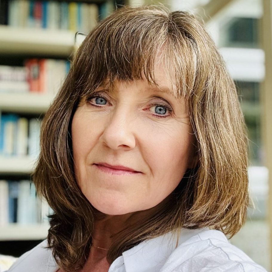 Angela Joyce website owner A woman with shoulder-length hair sits on a yellow sofa, smiling.