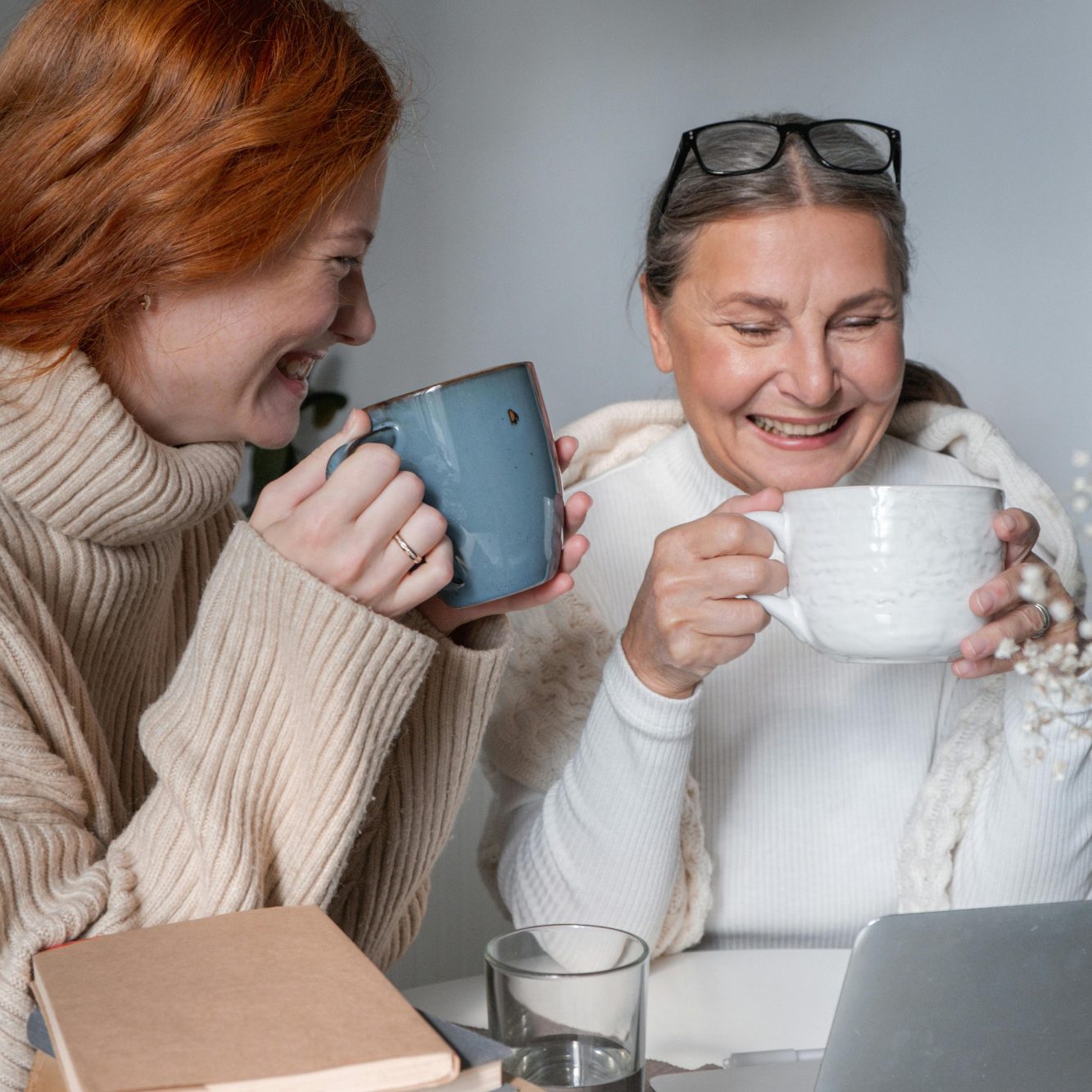 Peer Support for Neurodivergent Women Two women smiling and enjoying cups of tea while sitting at a table with a laptop.
