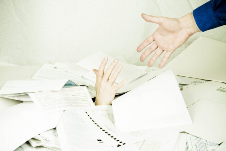 Photo: person drowning in paperwork, other person helping